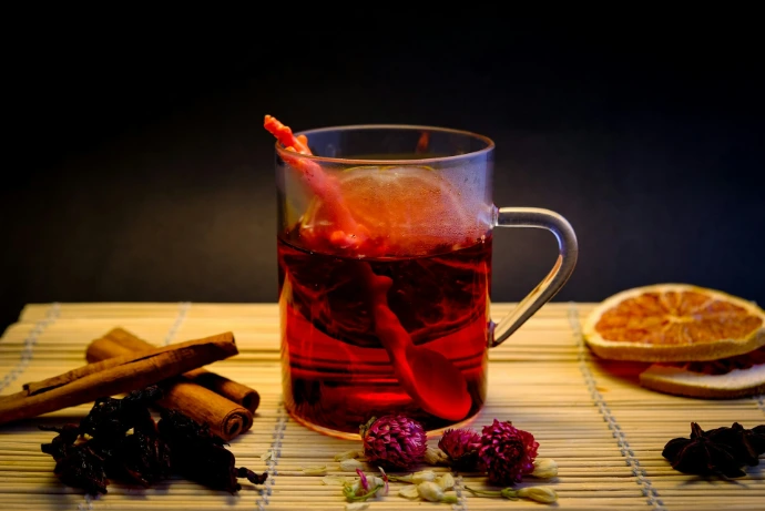 Glass mug with red beverage, cinnamon sticks, and dried fruit.