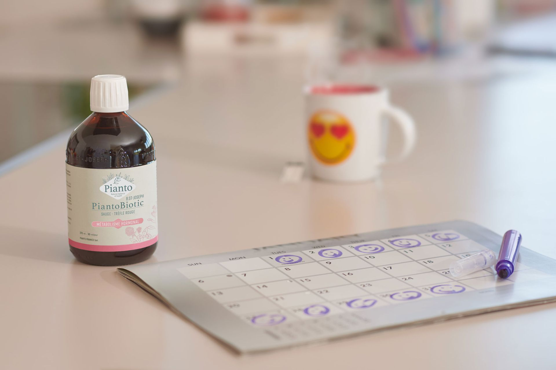 Bouteille de PiantoBiotic O Féminin posée sur une table à côté d'un calendrier et d'une tasse avec un smiley et des yeux en coeur