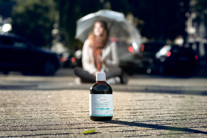 Jeune fille assise avec un parapluie devant une bouteille de PiantoBiotic Défenses Naturelles