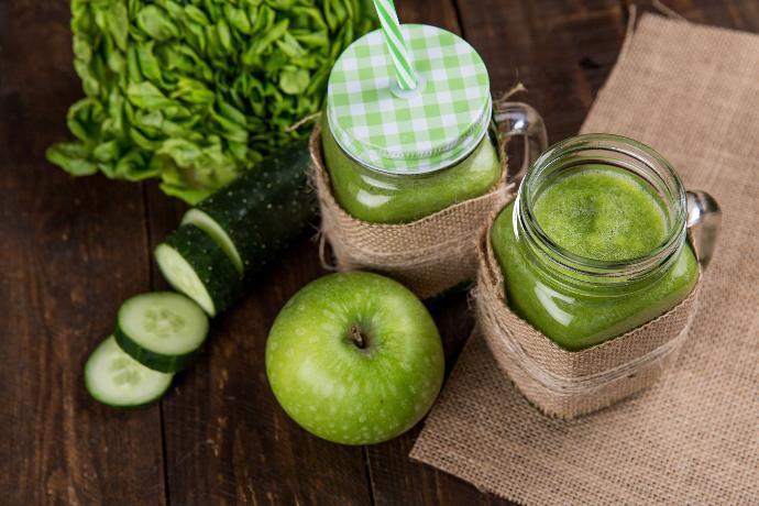 Photo de smoothie au PiantoBiotic. 2 smoothies verts sont posés sur une table à côté d'une pomme, d'un concombre et d'une salade 
