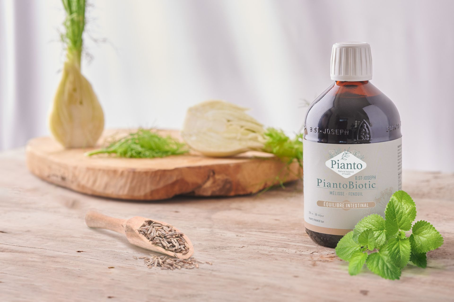 Bouteille de PiantoBiotic (Ex B.St-Joseph) Equilibre Intestinal sur une table à côté d'une branche de mélisse, d'un fenouil coupé un deux sur une planche en bois