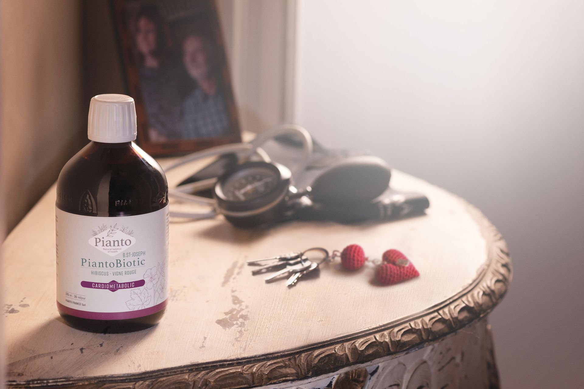 Bouteille de PiantoBiotic (Ex B.St-Joseph) sur une table à côté d'un trousseau de clé en forme de cœur, un stéthoscope et un cadre avec la photo d'un couple âgé d'une soixantaine d'années 