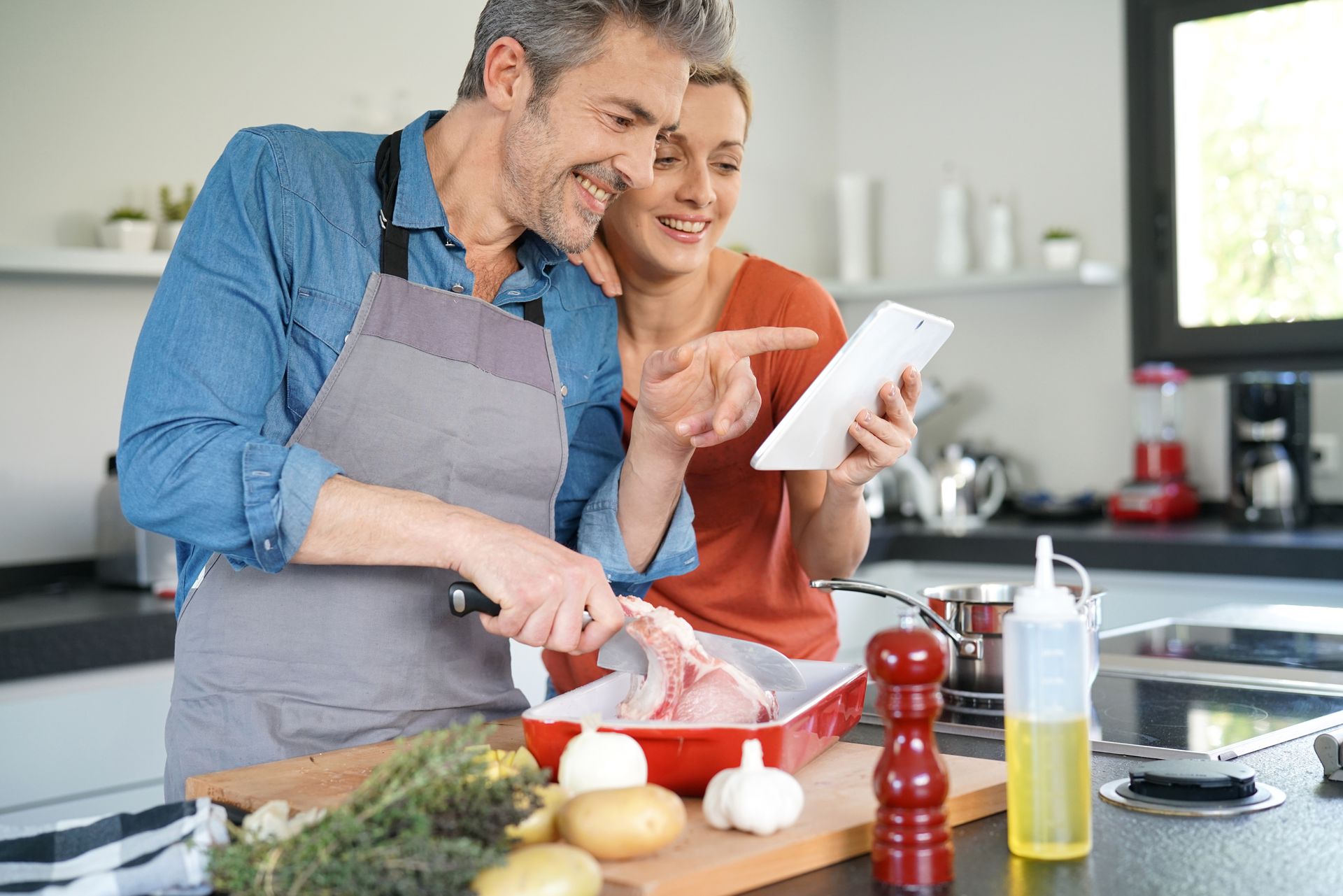 Couple dans une cuisine occupés à cuisiner un repas sain tout en regardant une recette sur une tablette
