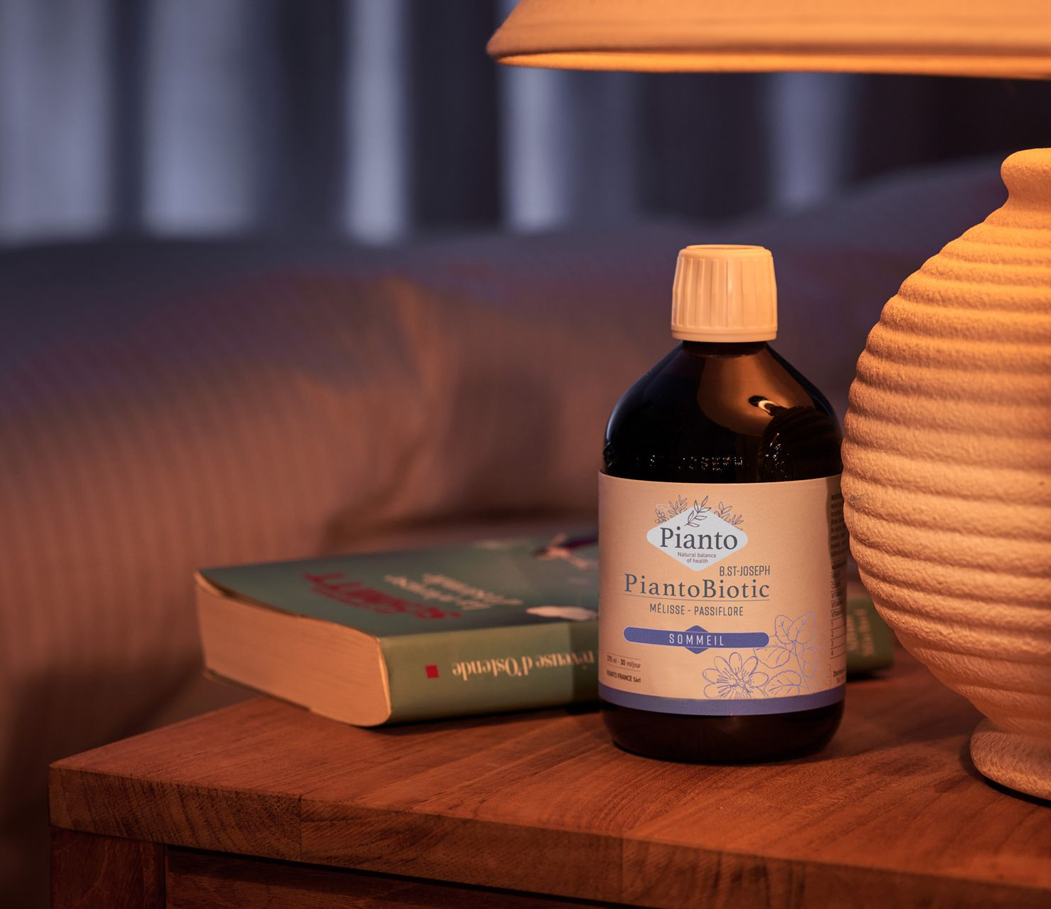 Flacon de PiantoBiotic SOMMEIL sur une table basse à côté d'un livre et une lampe de chevet