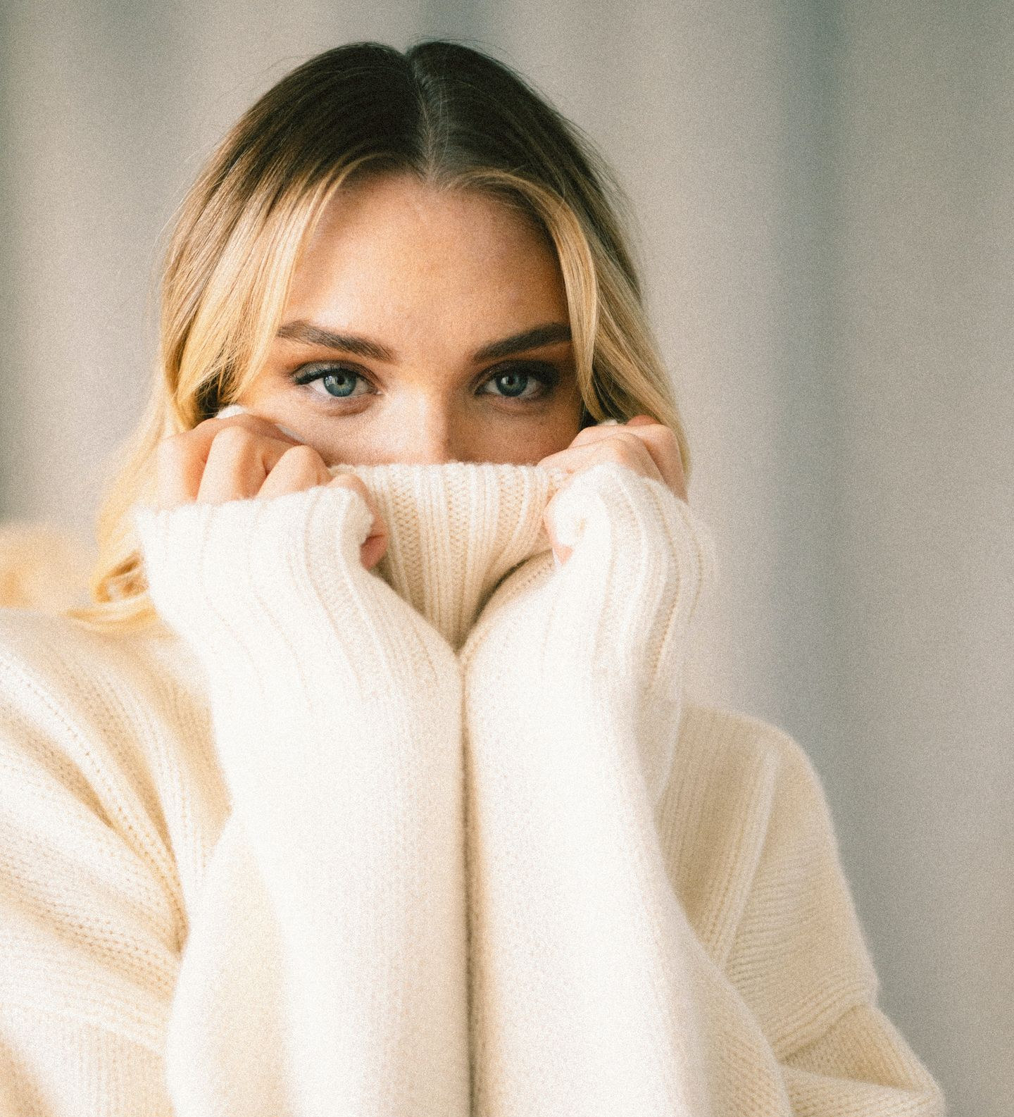 Jeune femme blonde qui remonte le col de son pull en laine jusqu'au dessus dunez