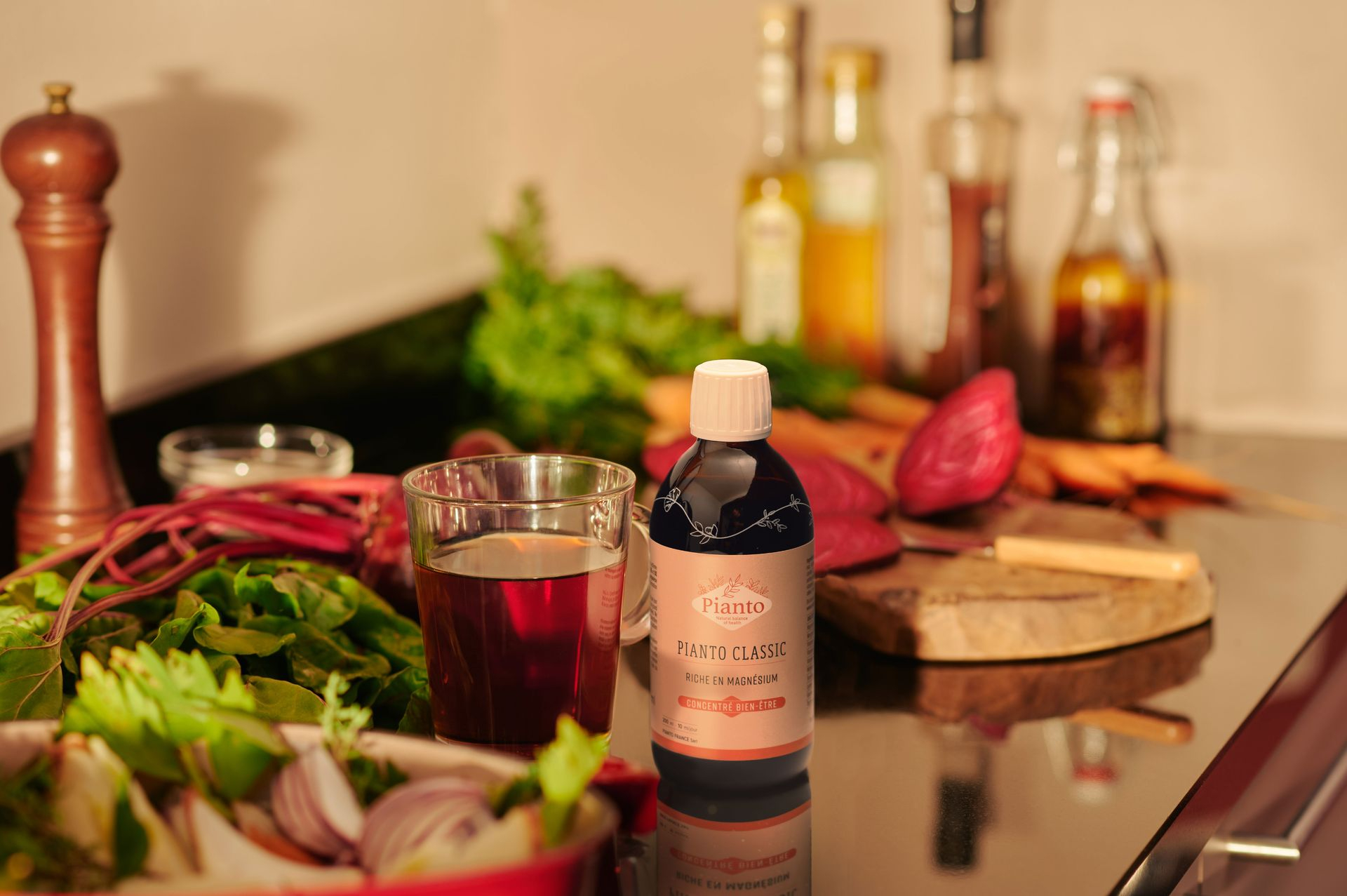 Flacon de Pianto CLASSIC dans une cuisine à côté d'un verre de jus de betterave et de légumes