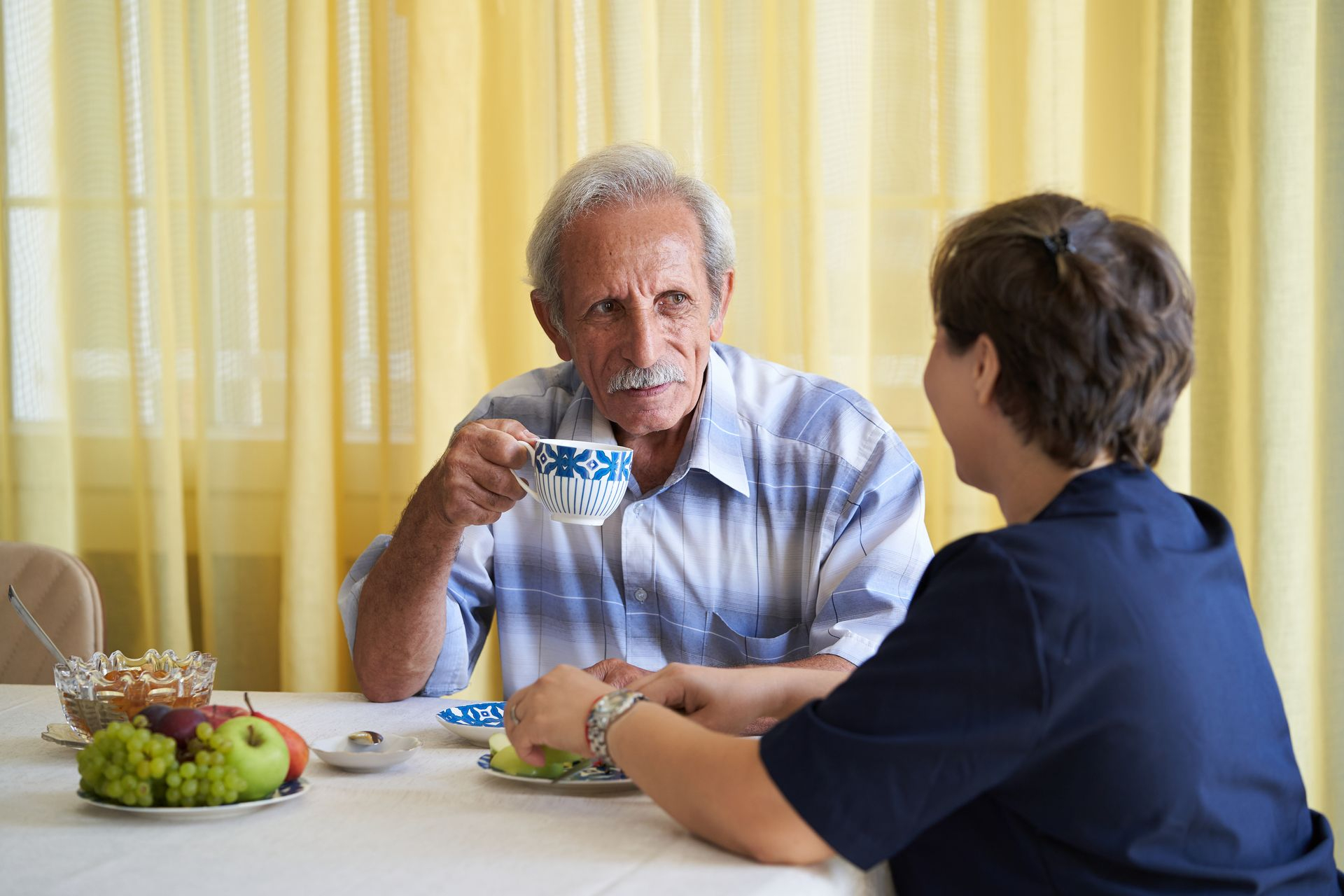 Homme âgé à table qui boit  dans une tasse en discutant avec une jeune femme