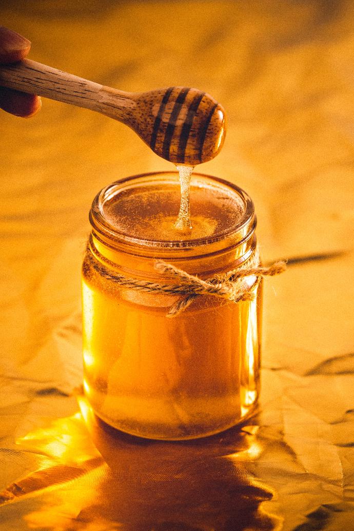 Cuillère en bois en forme de ruche au-dessus d'un pot de miel