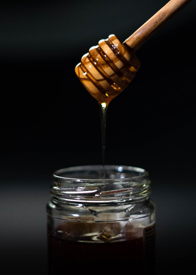 Cuillère en bois en forme de ruche au-dessus d'un pot de miel 