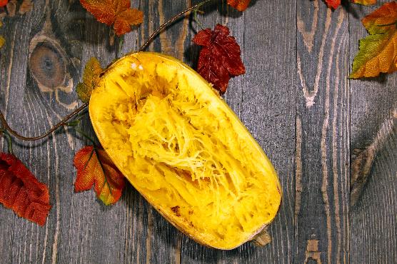 Demi courge spaghetti sans garniture posée sur une table en bois foncée, décorée par des feuilles d'automne 