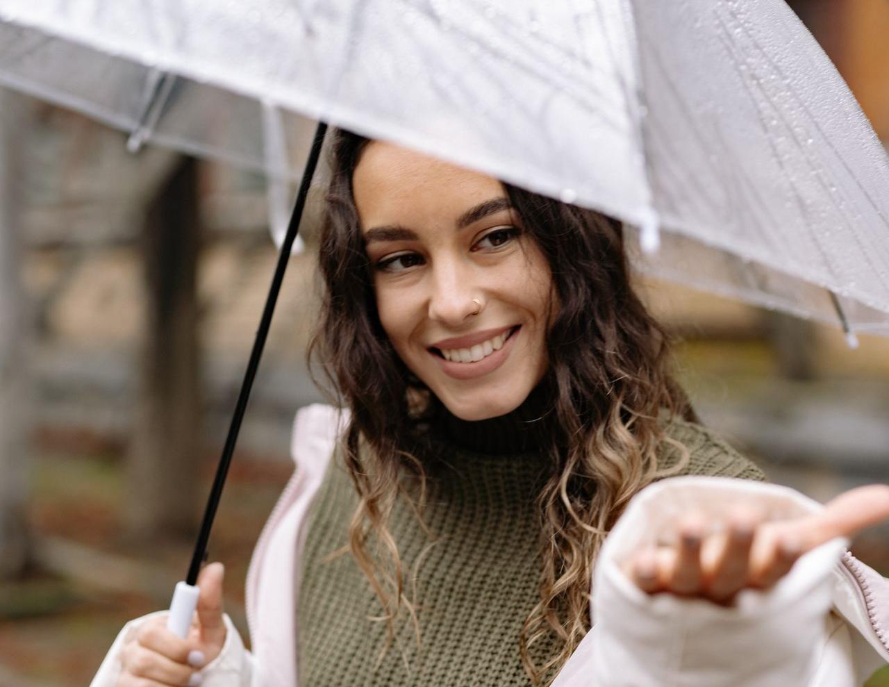 Jeune femme souriante avec un parapluie sous la pluie 