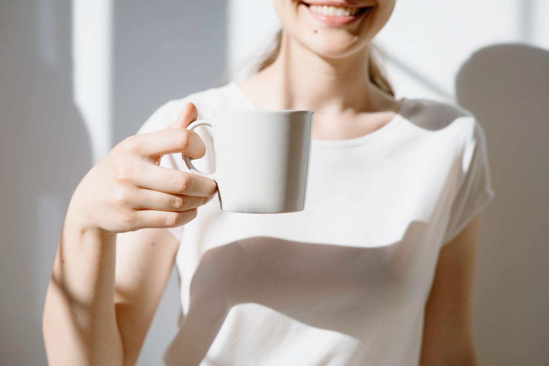 Jeune femme souriante, habillée en blanc qui tient une tasse blanche dans sa main